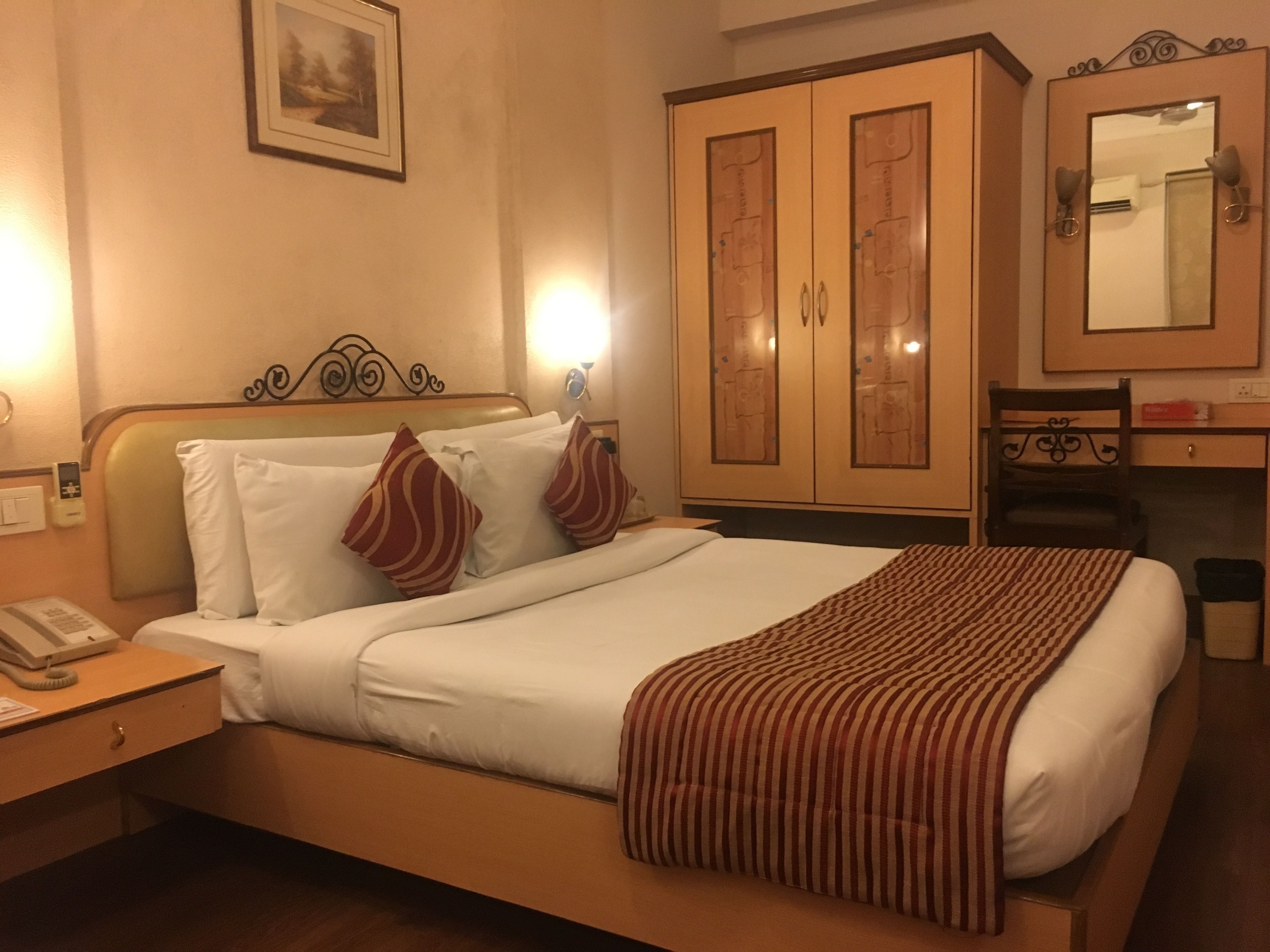 Una habitación de hotel con cama, escritorio, silla, armario y espejo.