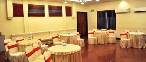 A banquet hall with round tables and chairs, a chandelier, and wall decorations.