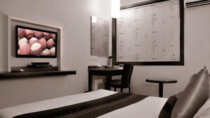 A hotel room with a bed, a desk, a chair, a small table, a television, and decorative wall panels. - Abbott Hotel (Navi Mumbai)