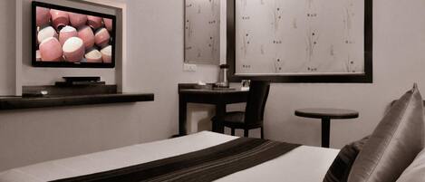 Una habitación de hotel con cama, escritorio, silla, una mesita, televisor y paneles decorativos en la pared.