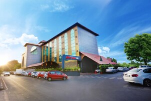 A hotel with a modern design, featuring a prominent entrance and a parking lot with several cars.