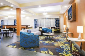 A hotel lobby with a seating area, a dining section, and a reception desk.