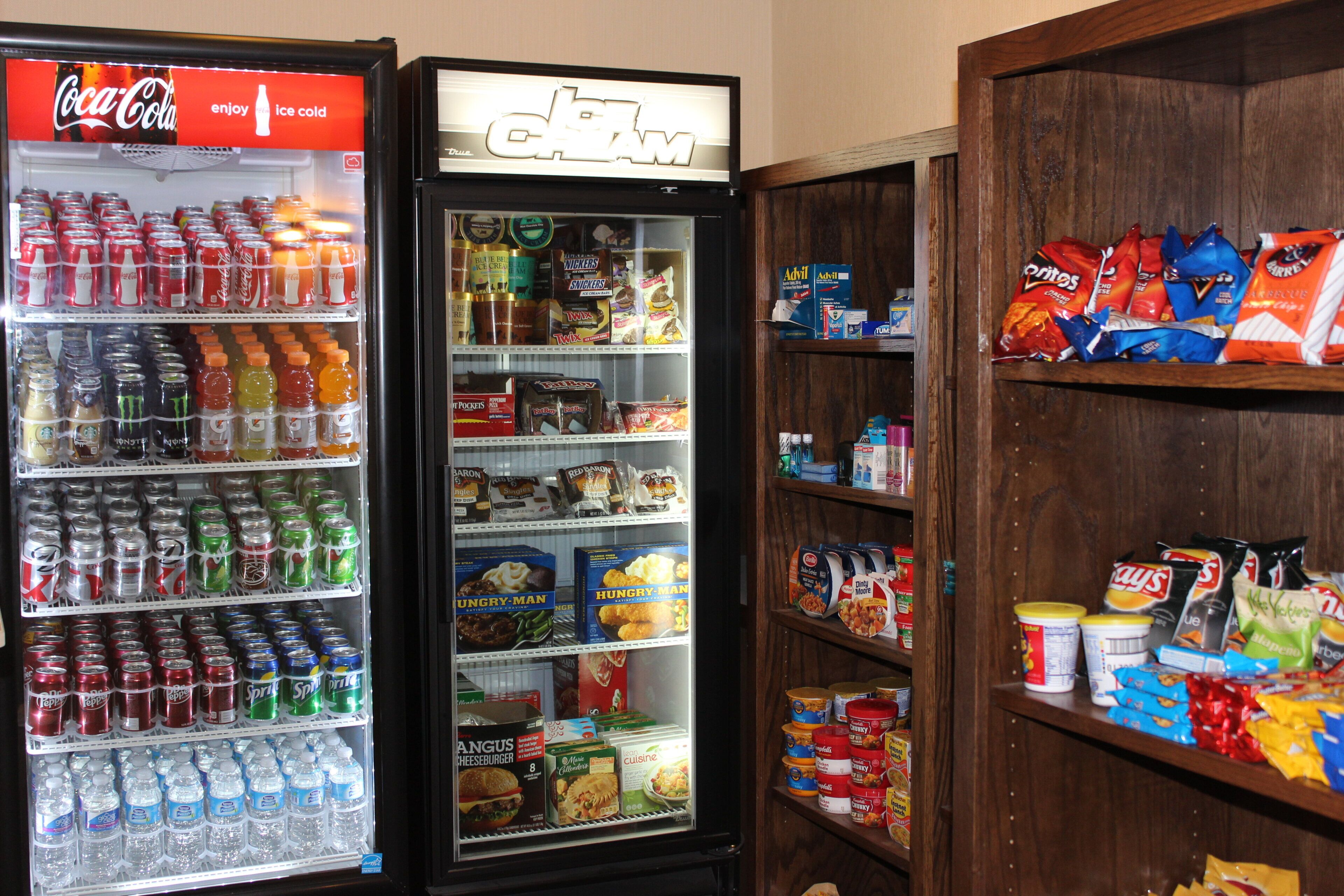 A vending machine with various snacks and drinks, a refrigerator with beverages, and shelves with packaged goods.