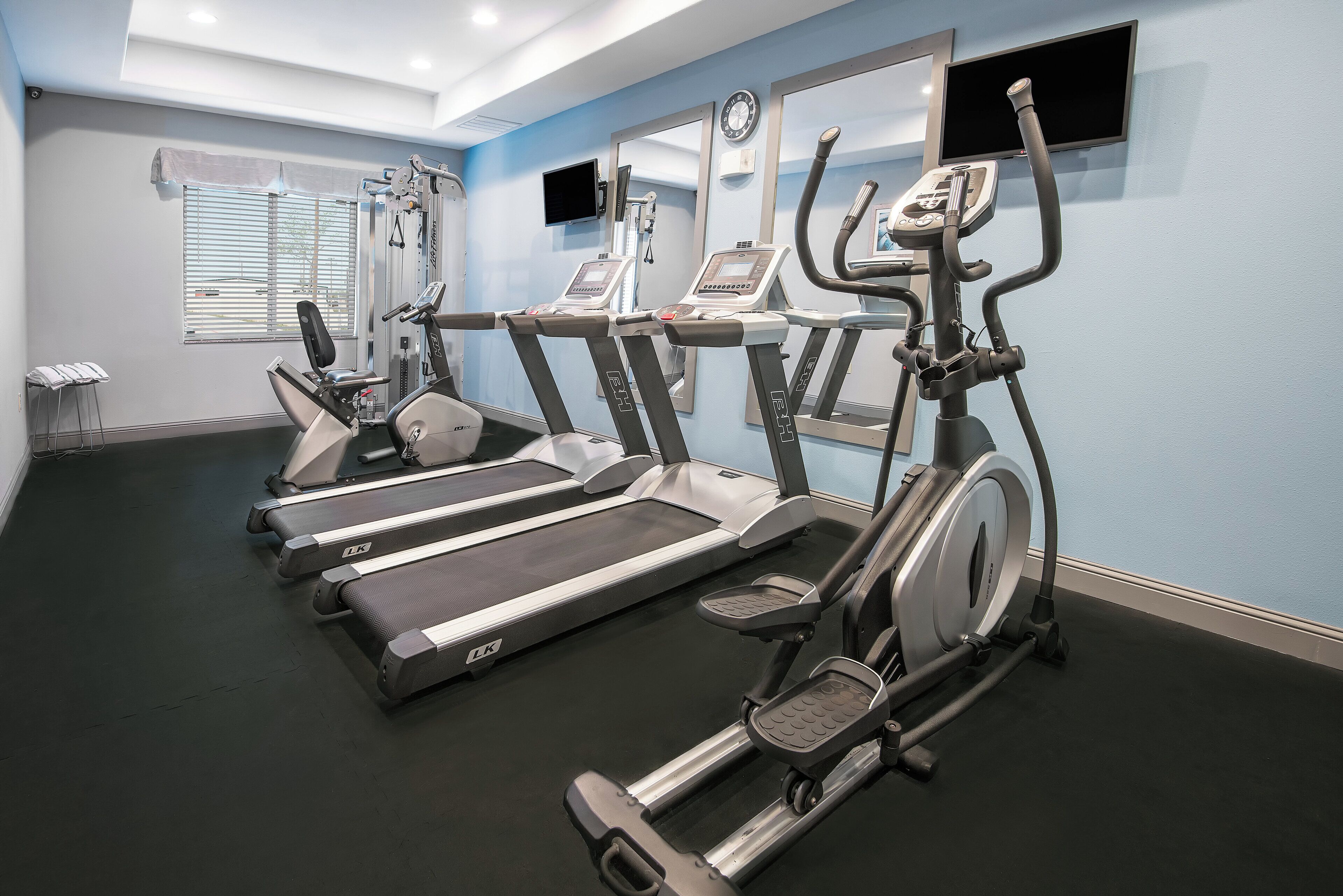A gym with multiple treadmills, ellipticals, and a wall-mounted TV.