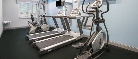 Un gimnasio con varias cintas de correr, elípticas y un televisor instalado en la pared.