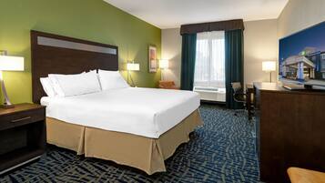 A hotel room with a large bed, two bedside tables with lamps, a desk with a chair, a television, and a window with curtains.