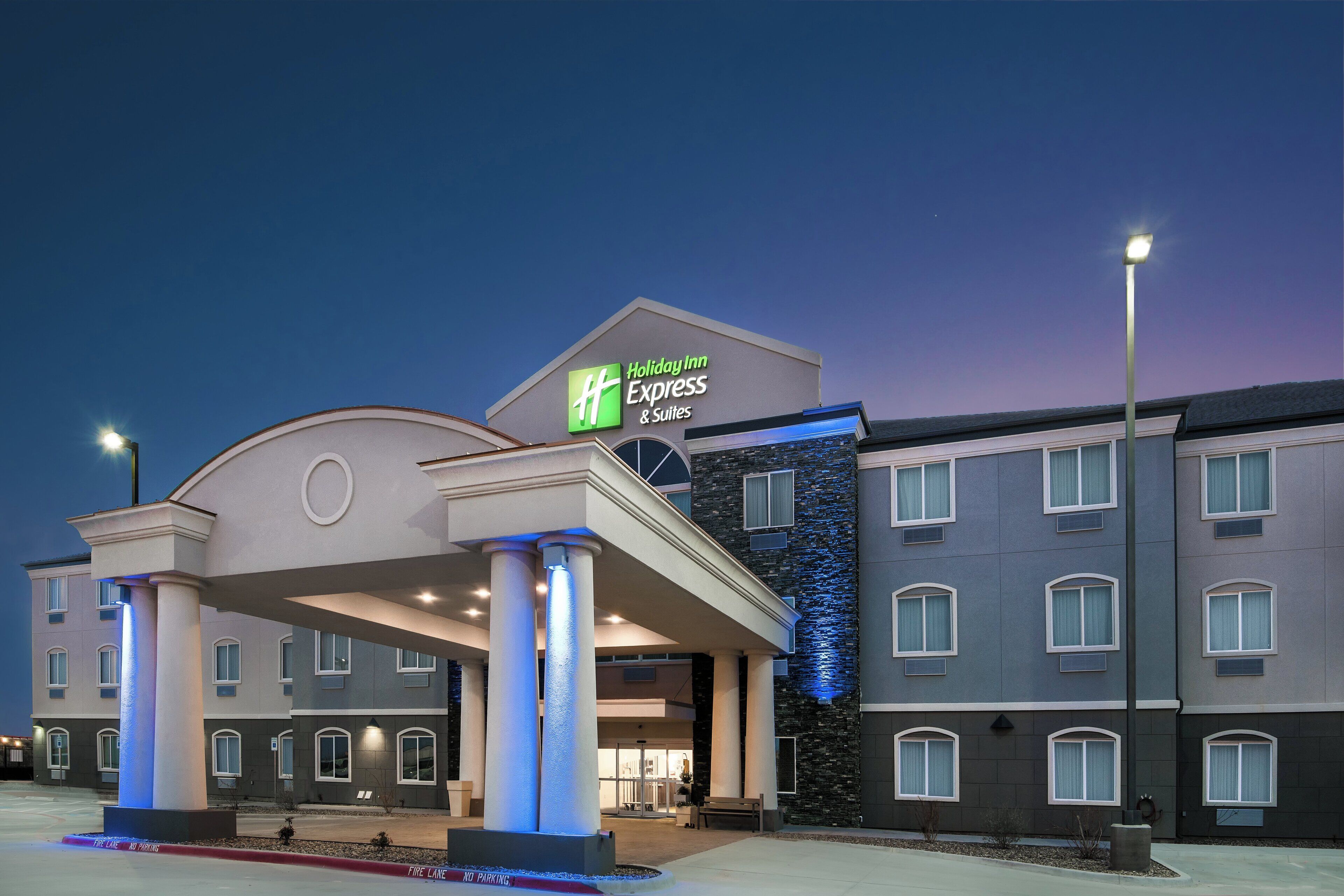 A Holiday Inn Express & Suites hotel with a modern facade, large columns, and a stone accent wall.