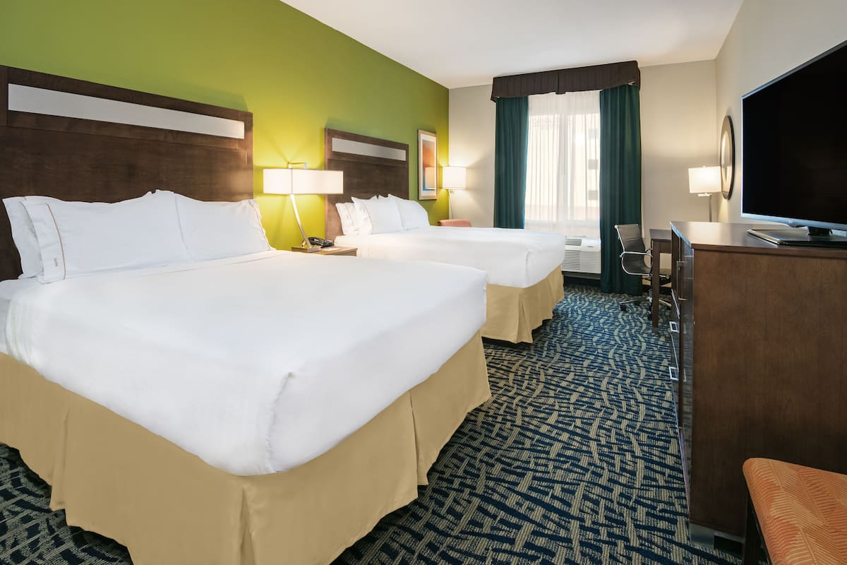 A hotel room with two beds, a desk, a TV, and a window with curtains.