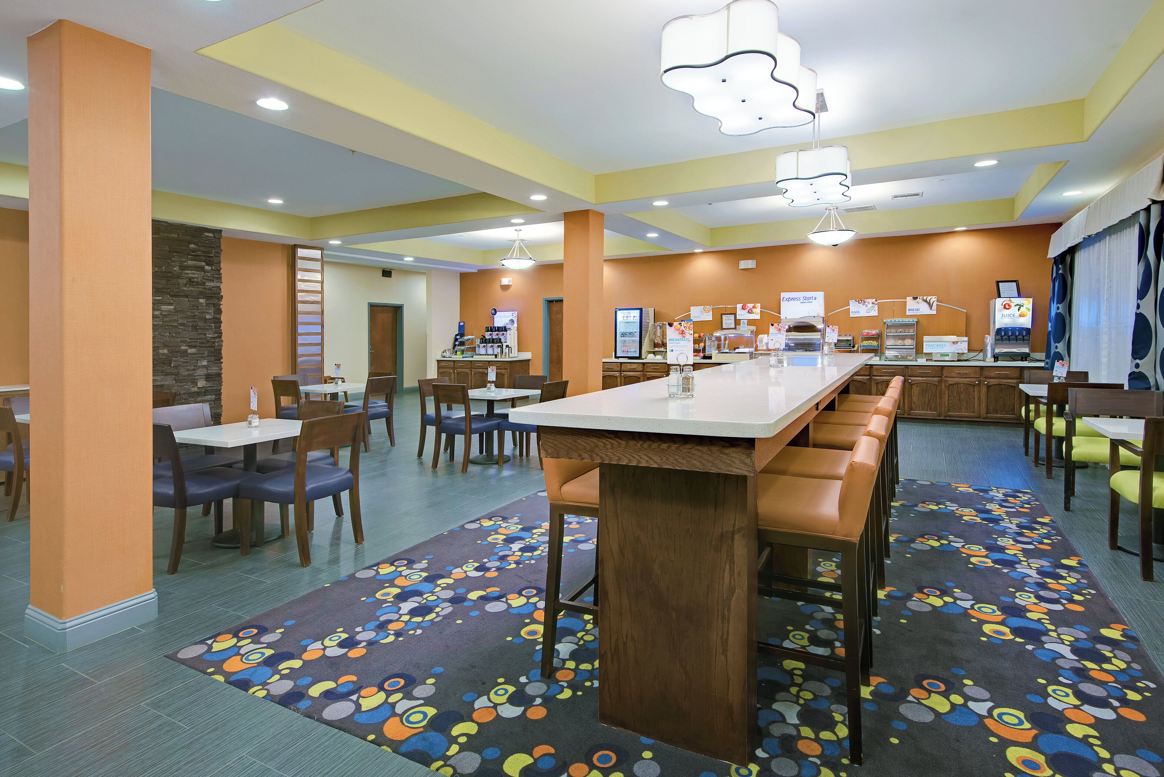 Zona de dinning d'un hotel amb bar central, seients a cabines i barra de buffet per esmorzar, amb diverses opcions de menjar.