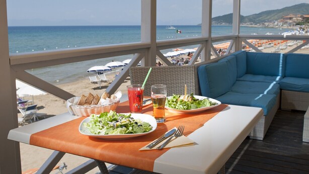 A dining table with a view of the beach, a wicker chair, and a blue sofa. - Hotel Paradiso Residence (Castellabate)