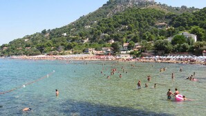 A beach with clear water, people swimming and sunbathing, and a hill with buildings in the background. - Hotel Paradiso Residence (Castellabate)