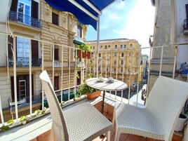 Un balcon agrémenté de meubles en osier, d’une table et de plantes suspendues.