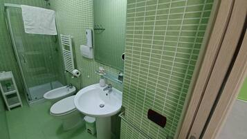 A bathroom with a shower, two toilets, a sink, and a mirror.