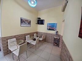 Zona pranzo con tavoli e sedie rotonde, una televisione a muro e un quadro incorniciato.