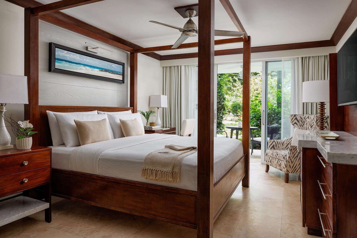 A four-poster bed with a ceiling fan, a television, and a view of the outdoors.
