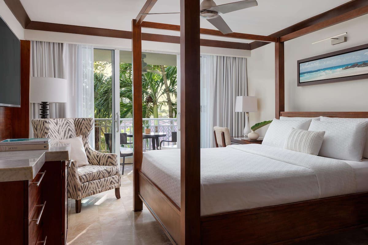 A hotel room with a large bed, a desk with a chair, a nightstand, and a view of the outdoors.