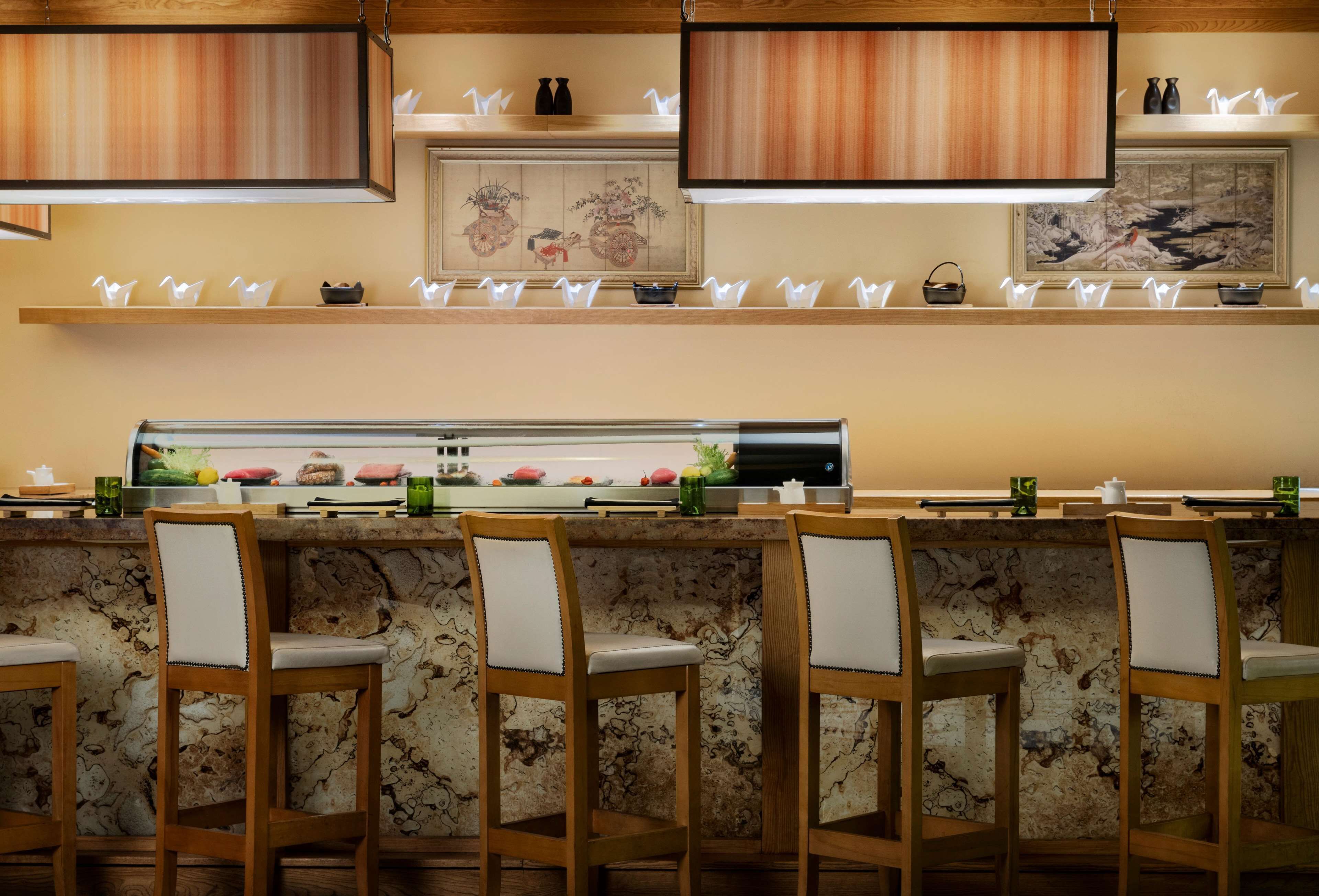 A restaurant with a marble countertop, wooden chairs, and a sushi bar.