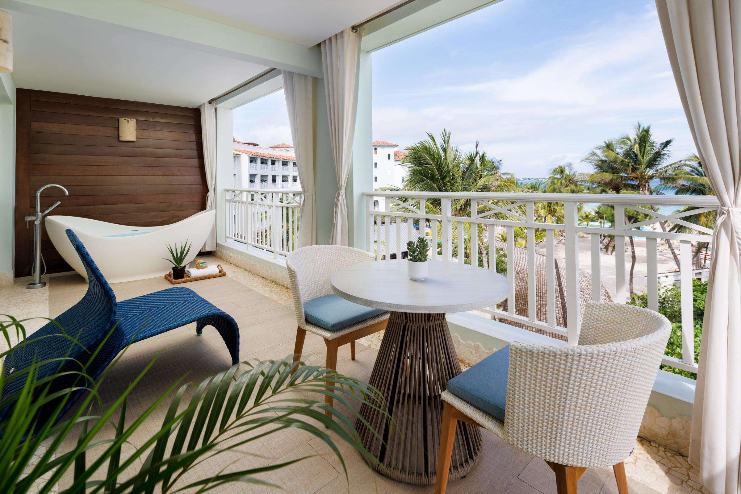 A balcony with a white wicker chair, a blue chair, and a round table.