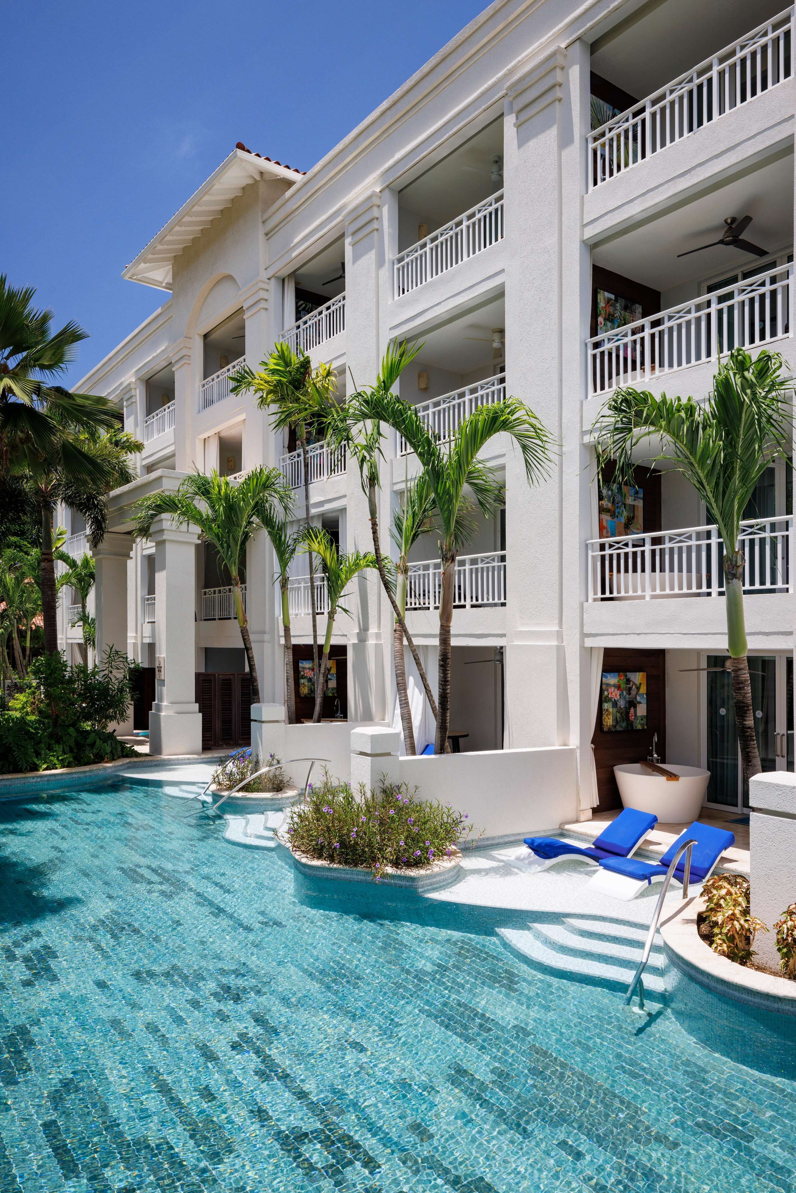 A hotel with a pool area, palm trees, and a white building facade.
