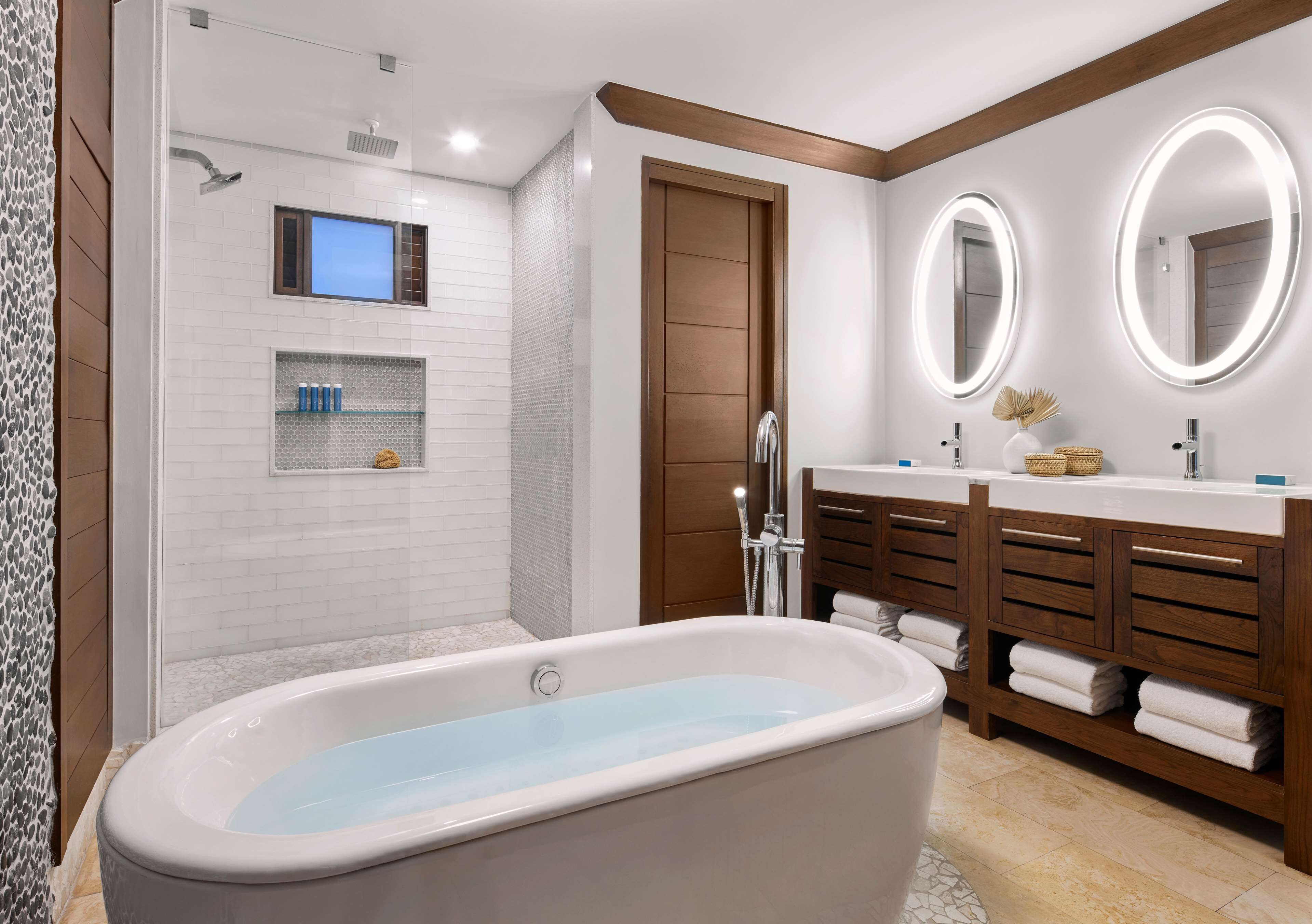A modern bathroom with a freestanding bathtub, a walk-in shower, and a vanity with a double sink and large mirrors.