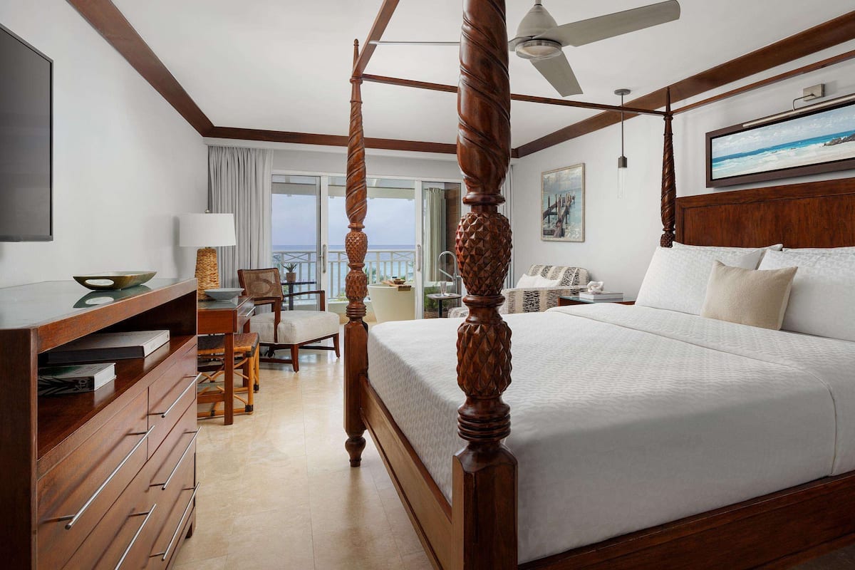 A four-poster bed with a wooden headboard, a television mounted on the wall, and a dining area with a table and chairs.