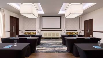 A conference room with a large screen, multiple tables with chairs, and a patterned carpet.