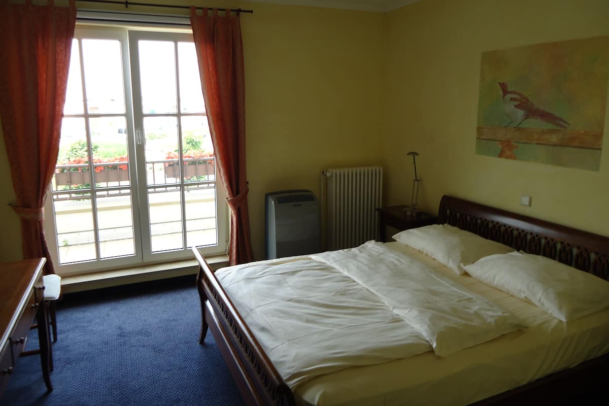 Ein Schlafzimmer mit einem Bett, einem Schreibtisch, einem Heizkörper und einem Fenster mit Vorhängen.