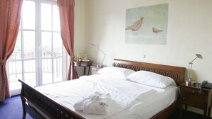 A neatly made bed with a wooden headboard, a bedside table with a lamp, and a painting of birds on the wall. - Hotel Landhaus Milser (Duisburg)