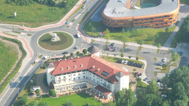 An aerial view of a hotel with a central courtyard, a roundabout, and a parking area. - Hotel Landhaus Milser (Duisburg)