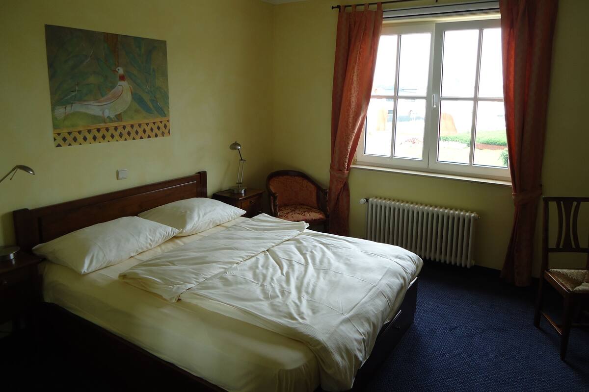 Ein Schlafzimmer mit Bett, Stuhl, Heizkörper und einem fenster mit Vorhängen.