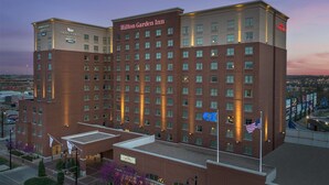 Un gran edificio de hotel con varios pisos, un letrero llamativo de Hilton Garden Inn y varias banderas, incluyendo la bandera estadounidense.
