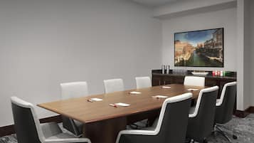 A conference room with a long wooden table, six grey chairs, a large painting of a cityscape, and a kitchen area with a marble countertop.