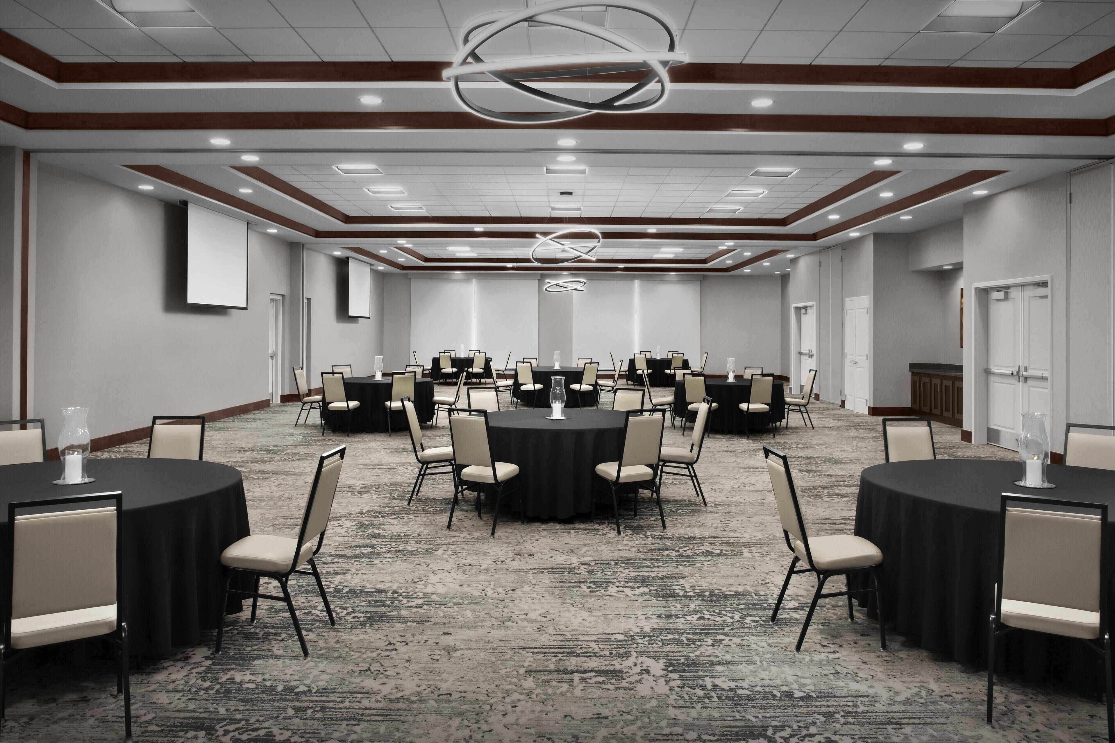 A conference room with multiple round tables, each surrounded by chairs, and a carpeted floor.