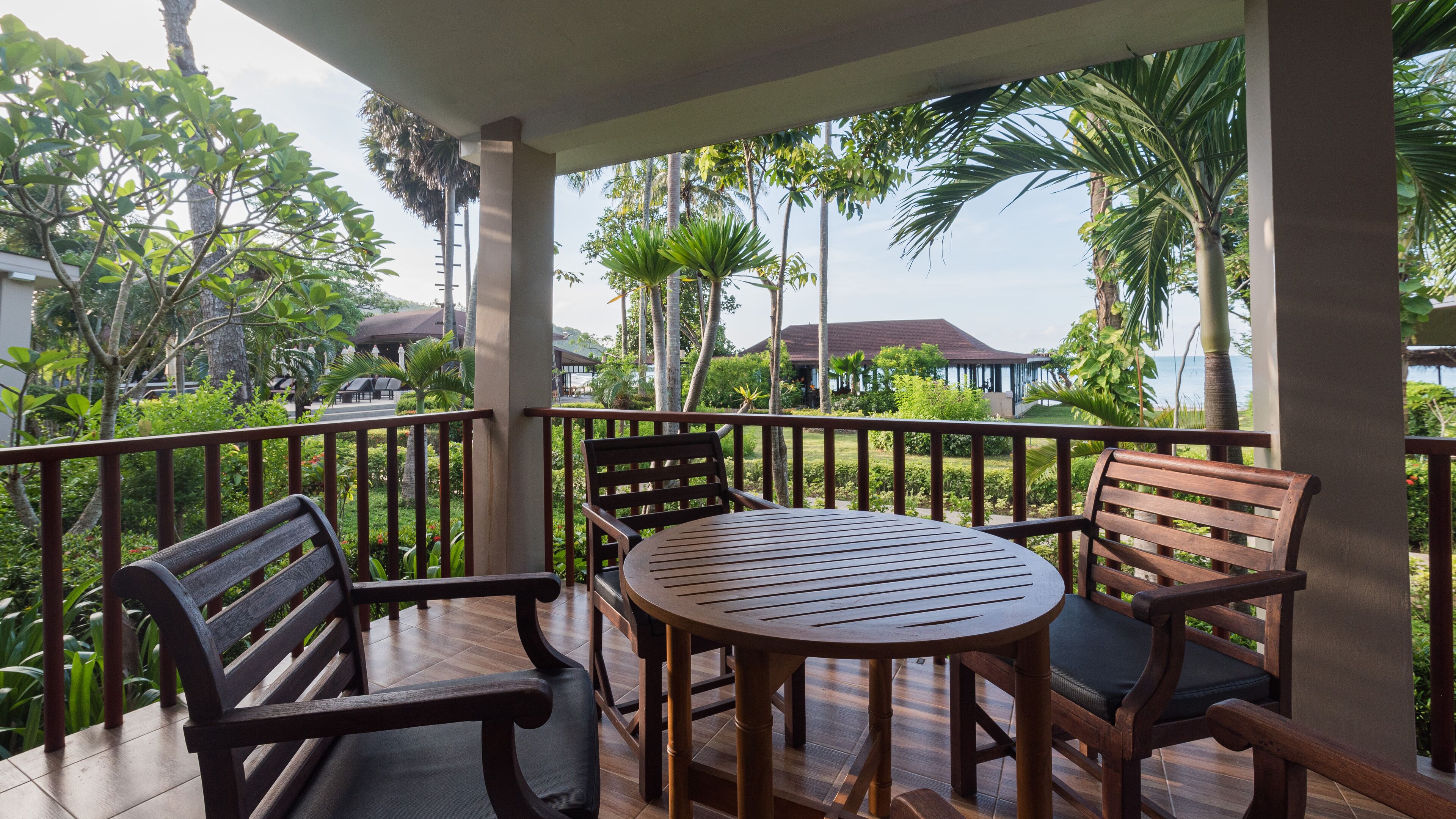 A wooden deck with a round table and two chairs, surrounded by a metal railing.