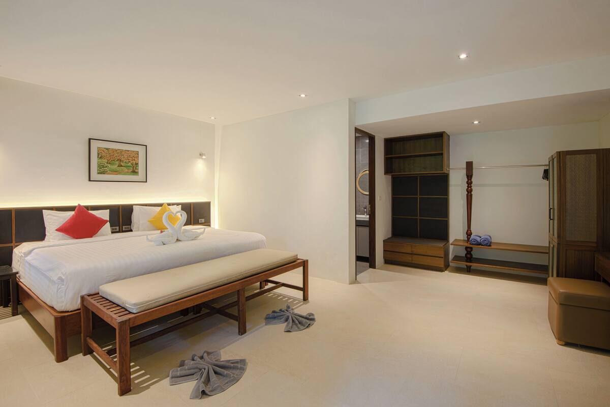 A modern hotel room with a large bed, a bench, a wooden headboard, a framed picture on the wall, and a walk-in closet.