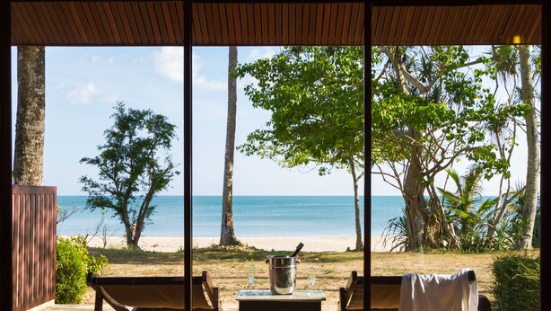 Une vue sur la plage depuis une terrasse couverte, avec une table, des chaises et un seau de champagne.