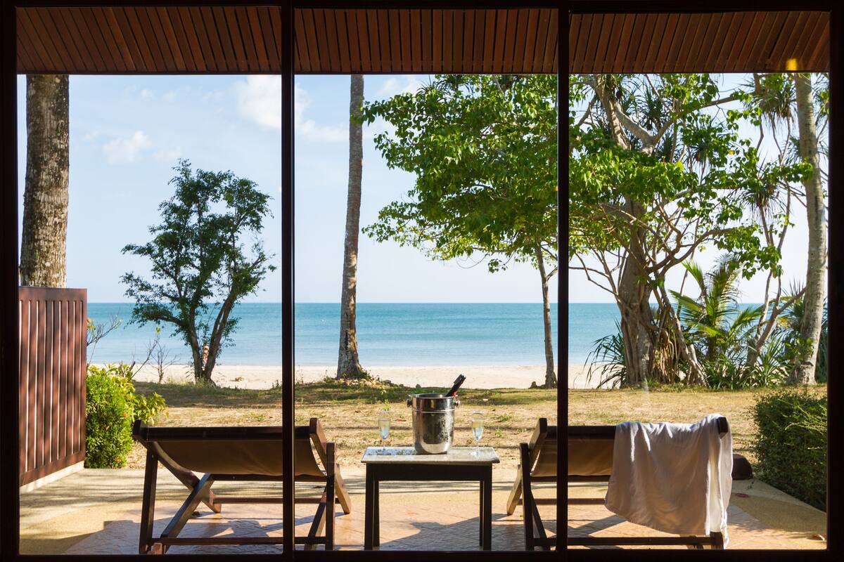 A beach view from a covered patio with a table, chairs, and a bucket of champagne.