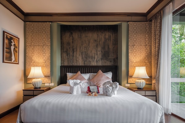 Une chambre d’hôtel avec un grand lit, deux lampes de chevet, une tête de lit en bois et une vue sur la verdure par la fenêtre.