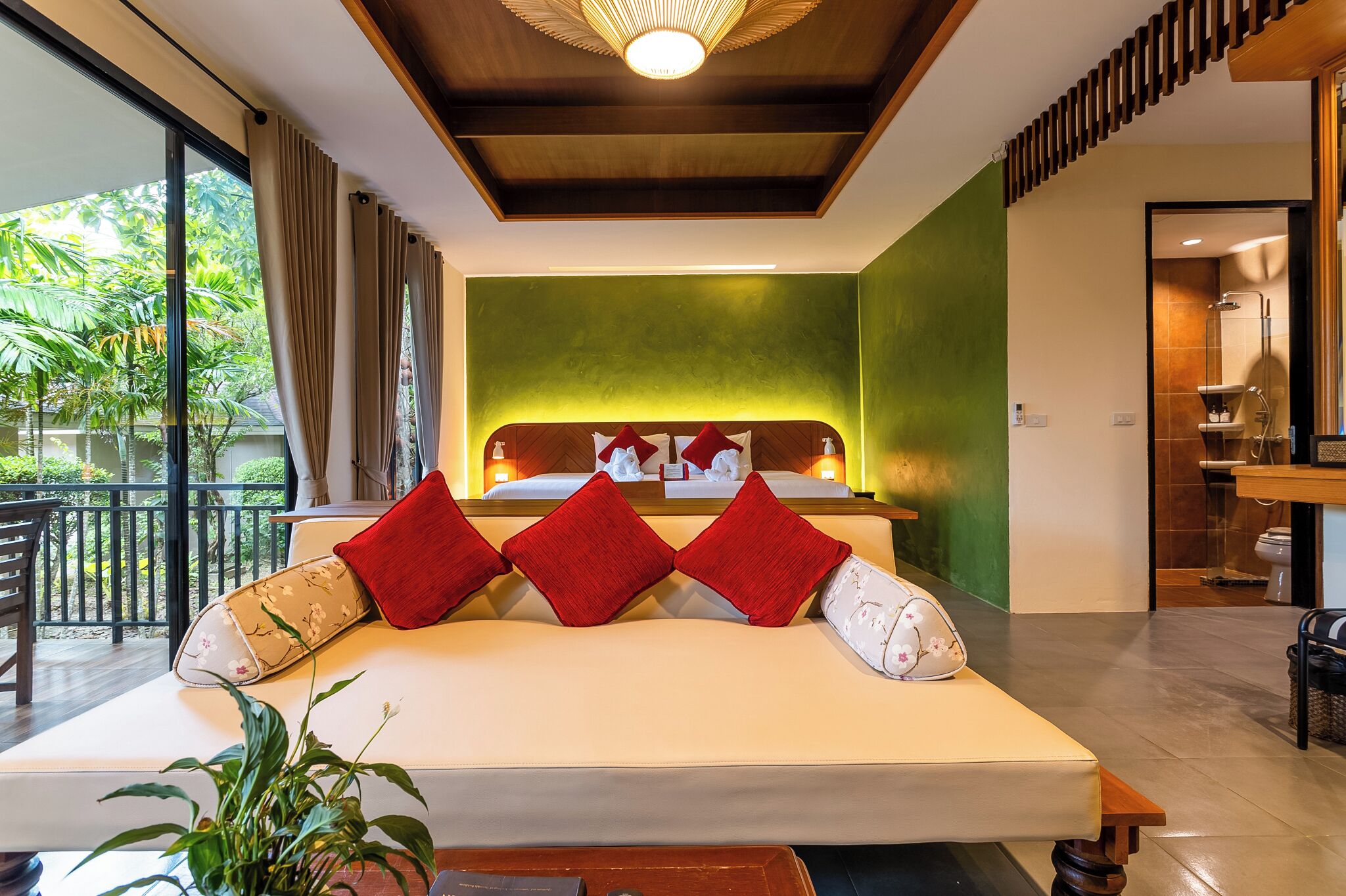 A modern hotel room with a large bed, a green accent wall, and a balcony with a view of greenery.