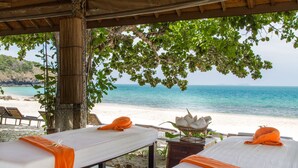 Un spa situé en bord de mer, équipé de deux tables de massage, chacune agrémentée d’une serviette orange et d’un linge blanc.
