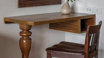A wooden desk with a mirror above it, a vase with a plant, and a chair.