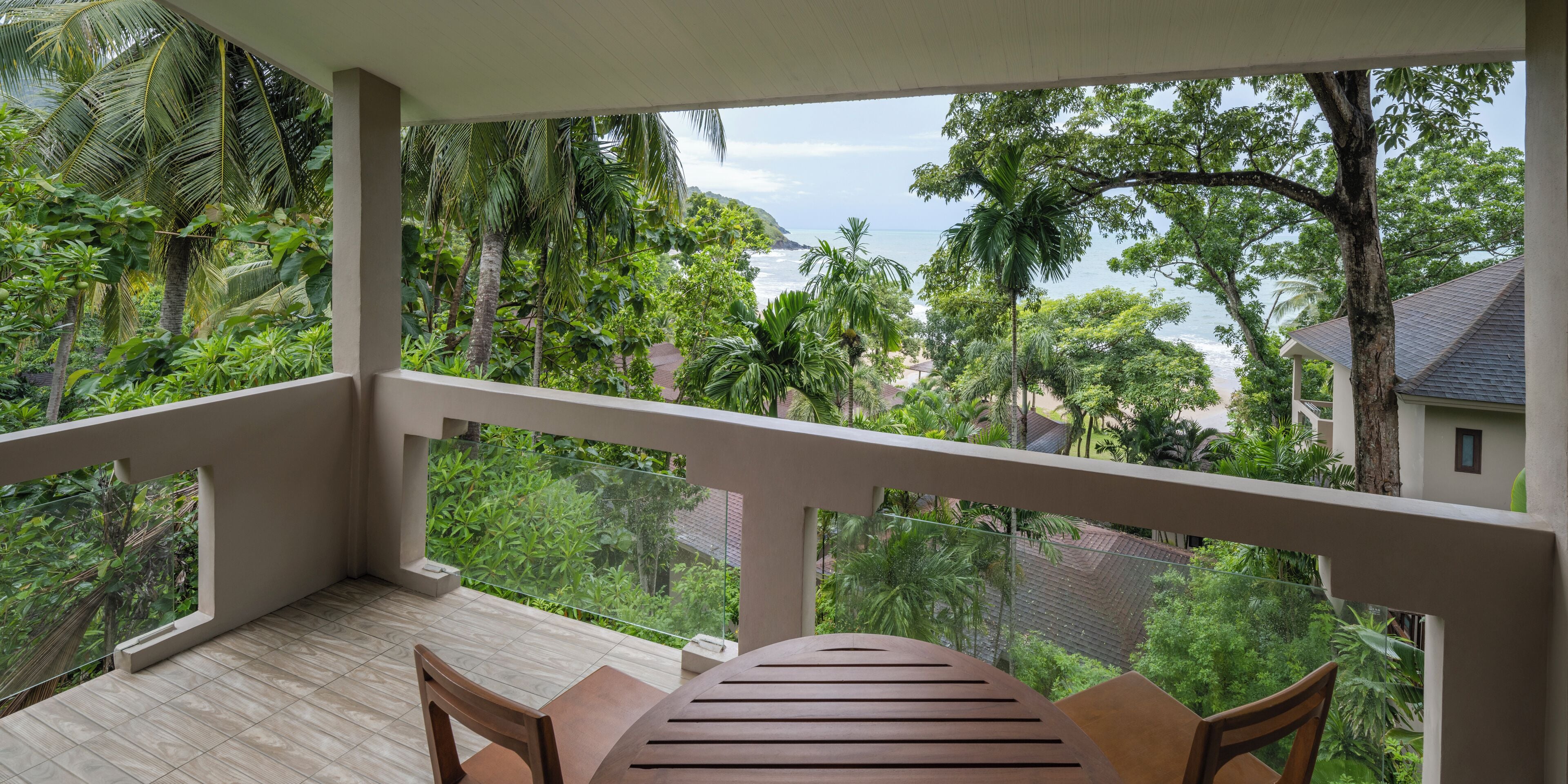 A balcony with a table and chairs, overlooking a lush garden and a view of the sea.