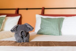 Una cama bien hecha con cabecera marrón, almohada verde y toalla gris doblada.