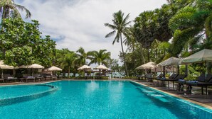 Une piscine d’un bleu éclatant, bordée de chaises longues et d’ombrelles, et entourée de palmiers.