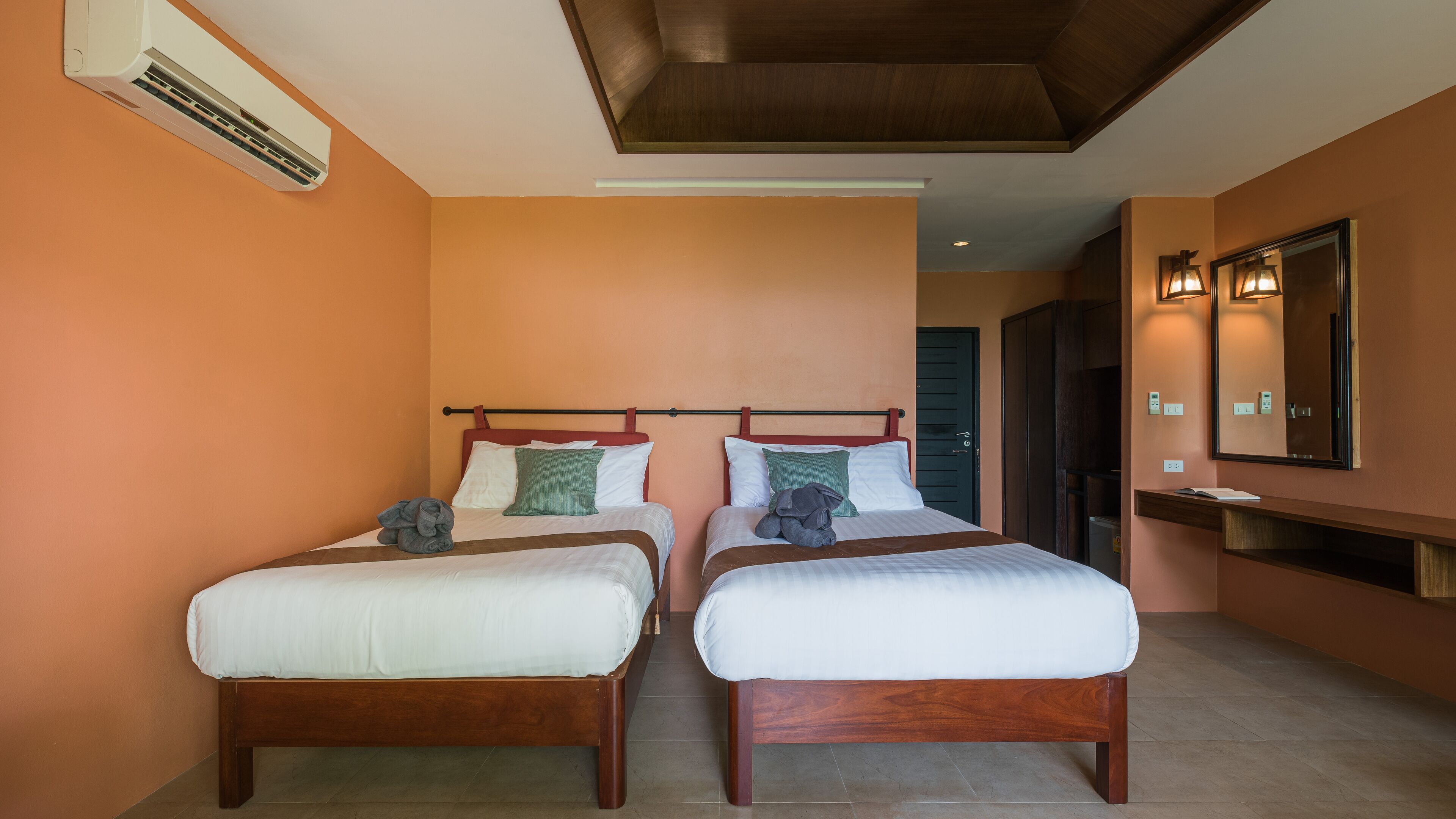 Habitació d'hotel amb dos llits de fusta, un mirall gran i un aparell d'aire condicionat.