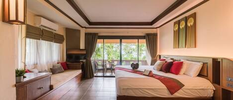 A hotel room with a large bed, a desk, and a balcony with a view of greenery.