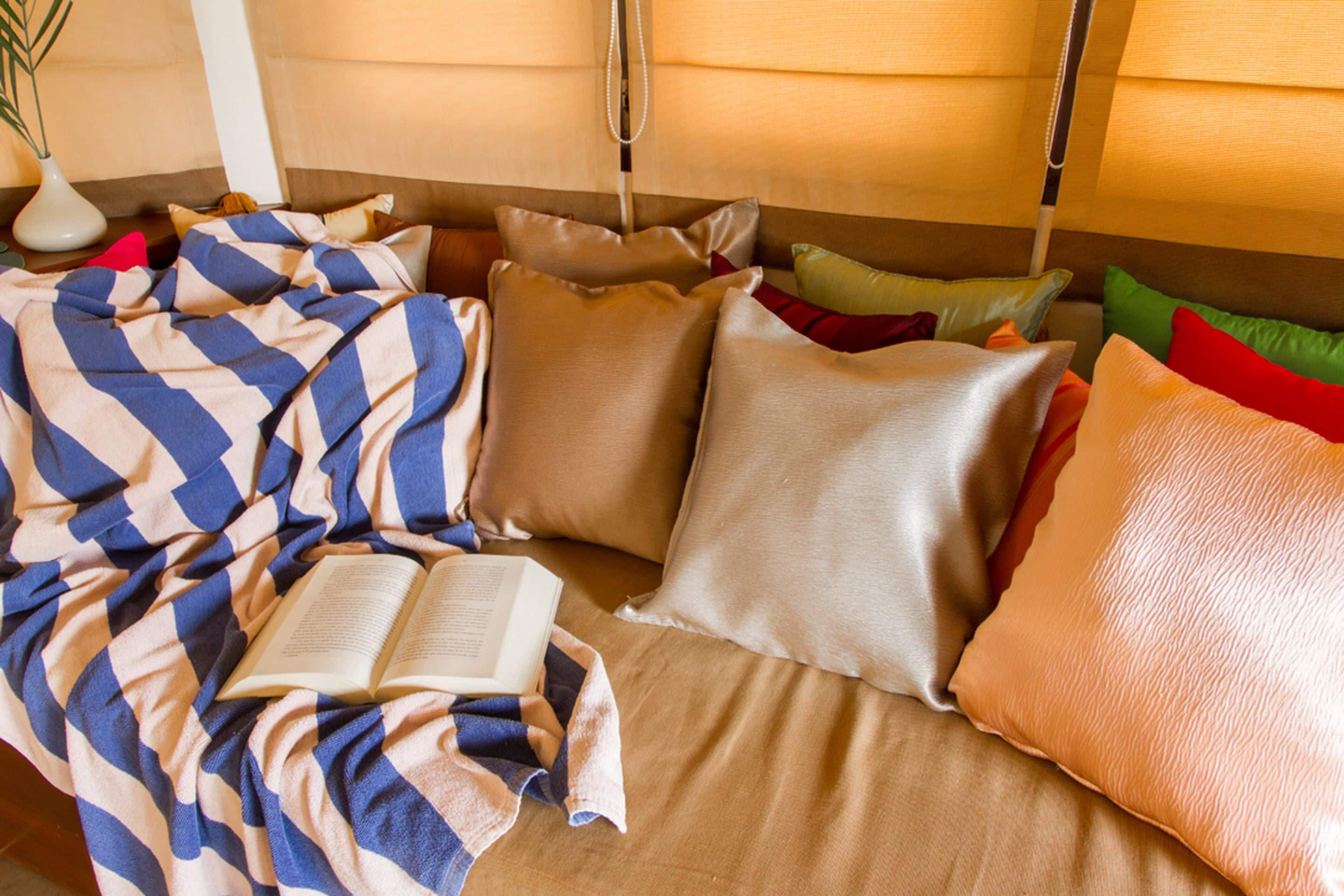 Una habitación acogedora con una cama cubierta por una colcha azul y blanca a cuadros, varios almohadones de distintos colores y un libro sobre la cama.