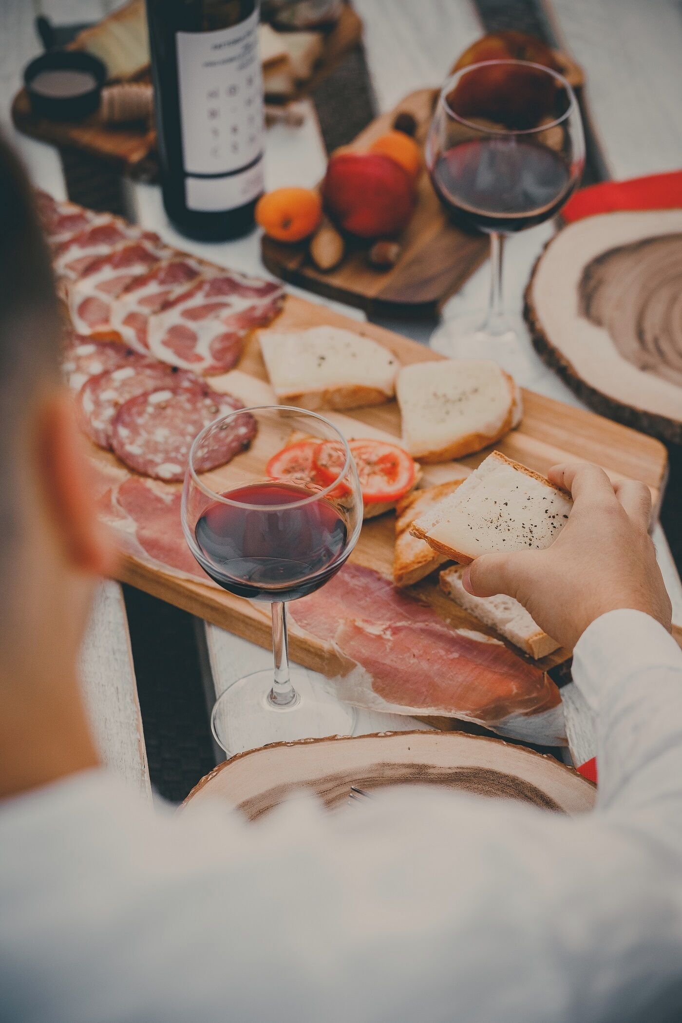Une table garnie de divers aliments, notamment des charcuteries, du pain et des tomates, ainsi que des verres de vin rouge.