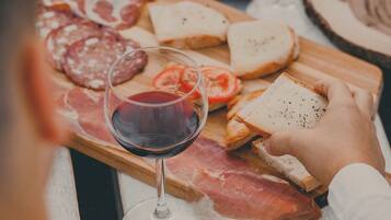 Une table garnie de divers aliments, notamment des charcuteries, du pain et des tomates, ainsi que des verres de vin rouge.