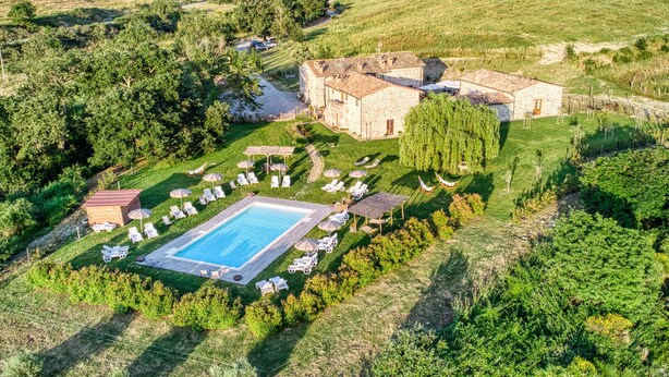 Vista aérea de una propiedad campestre con piscina, sillas de descanso y un edificio de piedra.